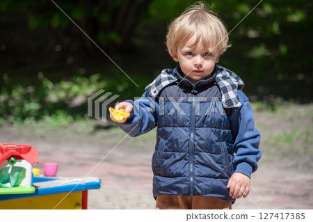 A young boy enjoys playing with sand and toys in a colorful outdoor sandbox on a sunny day. The scene showcases childhood play, creativity, and the joys of exploring outdoors. A young boy enjoys playing with sand and toys in a colorful outdoor sandbox on a sunny day. The scene showcases childhood play, creativity, and the joys of exploring outdoors. 127417385