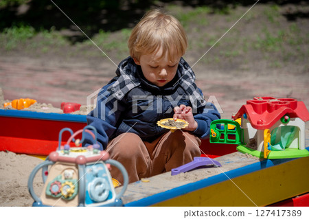A young boy enjoys playing with sand and toys in a colorful outdoor sandbox on a sunny day. The scene showcases childhood play, creativity, and the joys of exploring outdoors. A young boy enjoys playing with sand and toys in a colorful outdoor sandbox on a sunny day. The scene showcases childhood play, creativity, and the joys of exploring outdoors. 127417389