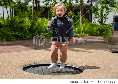 A young child jumping on a trampoline at an outdoor park surrounded by greenery. The child shows excitement and joy while playing, embodying youthful energy and fun in the sunlit environment. A young child jumping on a trampoline at an outdoor park surrounded by greenery. The child shows excitement and joy while playing, embodying youthful energy and fun in the sunlit environment. 127417435