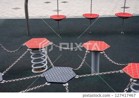 Modern playground apparatus with hexagonal platforms, springs, and chains, designed for children outdoor activity and fitness. The durable materials and vibrant colors enhance the play experience. Modern playground apparatus with hexagonal platforms, springs, and chains, designed for children outdoor activity and fitness. The durable materials and vibrant colors enhance the play experience. 127417467