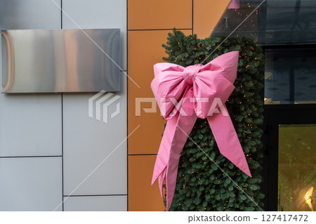 A large pink bow decorates a holiday scene with festive lights and green foliage, evoking holiday cheer. Mockup, signboard 127417472