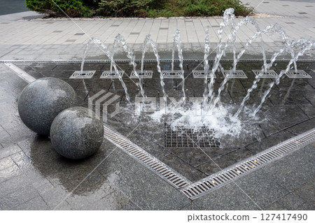 Outdoor decorative fountain with round marble sculptures and flowing water streams. 127417490