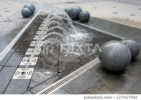 Outdoor decorative fountain with round marble sculptures and flowing water streams. 127417492