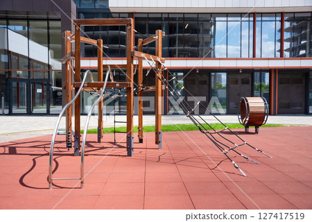 Outdoor playground structure featuring wooden and rope elements in a modern urban setting, activities for children in a safe environment. Enclosed by apartment buildings, perfect for families to enjoy 127417519