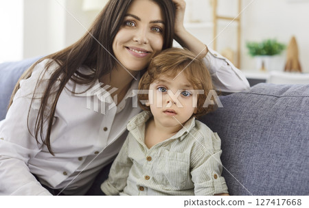 Happy young woman cuddling small kid son portrait, having fun together on couch in living room 127417668
