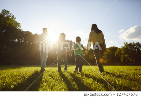 Family walking together in grassy green field, close holding hands towards sun Family walking together in grassy green field, close holding hands towards sun 127417676