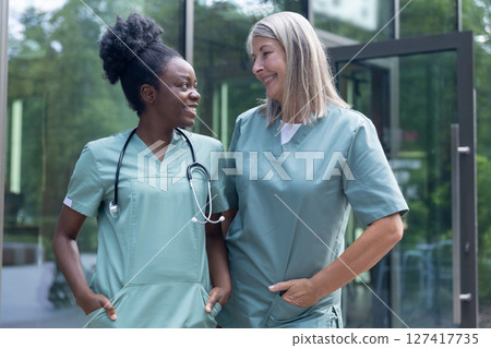 Two female doctors talking and looking contented and joyful Two female doctors talking and looking contented and joyful 127417735