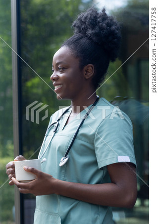 African american woman in a lab coat standing in the clinics door with a cup of coffee African american woman in a lab coat standing in the clinics door with a cup of coffee 127417758