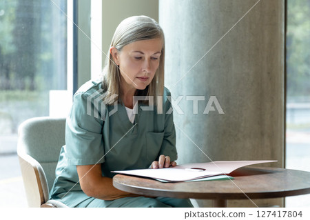 Blonde mature caucasian female doctor scrutinizing medical history Blonde mature caucasian female doctor scrutinizing medical history 127417804