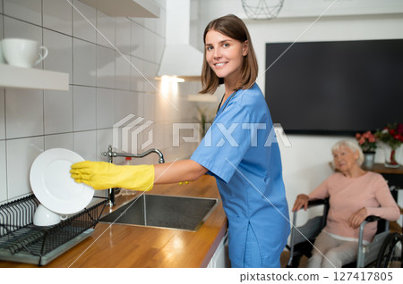 Young nurse cleaning the kitchen in the elderly woman house Young nurse cleaning the kitchen in the elderly woman house 127417805