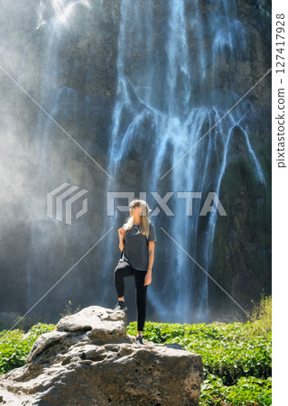 Young woman standing on a rock near majestic waterfall at sunset Young woman standing on a rock near majestic waterfall at sunset 127417928
