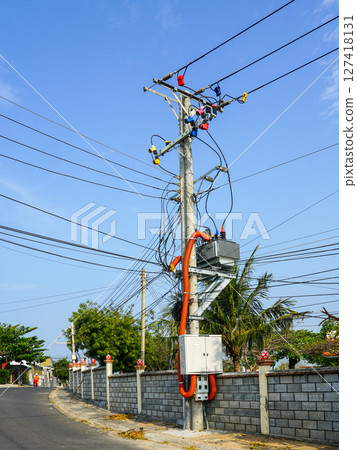 Street power pole with complex electric wiring and colorful connectors against a clear blue sky in Vietnam 127418131
