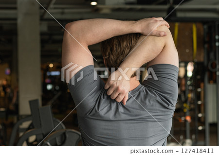 Athlete or caucasian young sporty man doing stretching back and arms at gym before workout. Training, wellness and athlete man workout. Preparation for exercise at health club. Back View 127418411