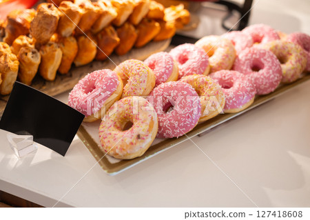 Colorful donuts with sprinkles on buffet table in hotel breakfast area. Sweet dessert, morning treat, and vibrant bakery presentation concept. 127418608
