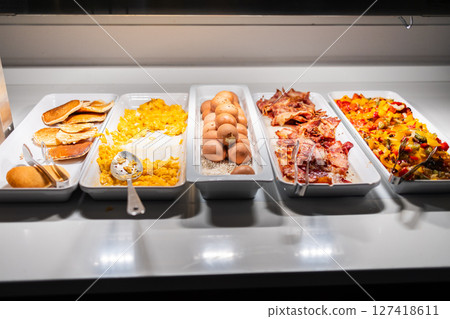 Hot breakfast buffet with eggs, pancakes, bacon, and vegetables. Morning meal variety, hotel catering, and colorful food presentation concept. 127418611