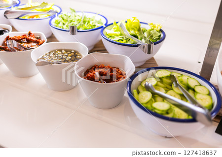 Fresh vegetables and toppings served in white bowls on buffet table. Healthy eating, salad bar variety, and hotel breakfast concept. Fresh vegetables and toppings served in white bowls on buffet table. Healthy eating, salad bar variety, and hotel breakfast concept. 127418637