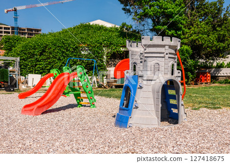 Colorful plastic playground with slides and castle structure on gravel. Outdoor recreation, children's fun zone, and imaginative play environment concept. 127418675