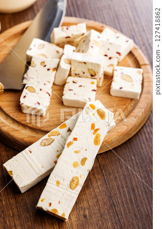 White nougat bars with almonds and dried fruit on cutting board on wooden table. 127418862