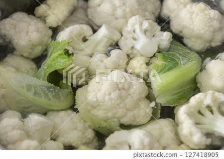 Fresh cauliflower is boiled in a water. The vegetable is divided into florets and boiled Fresh cauliflower is boiled in a water. The vegetable is divided into florets and boiled 127418905