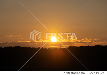 A stunning image capturing the glowing sun setting over a dark forest A stunning image capturing the glowing sun setting over a dark forest 127419174