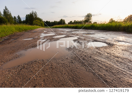 Scenic rural dirt road with reflective puddles from recent rain 127419179