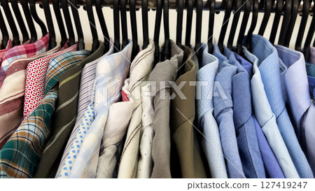 Many colorful men's shirts hang on hangers in the store. Men's wardrobe. Many colorful men's shirts hang on hangers in the store. Men's wardrobe. 127419247