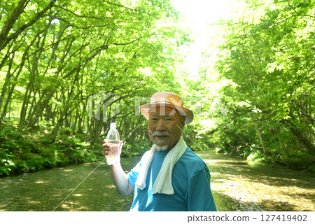 An old man hydrating in a mountain stream 127419402