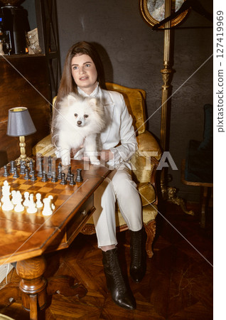 a girl sits at a table and holds a white dog in her arms 127419969