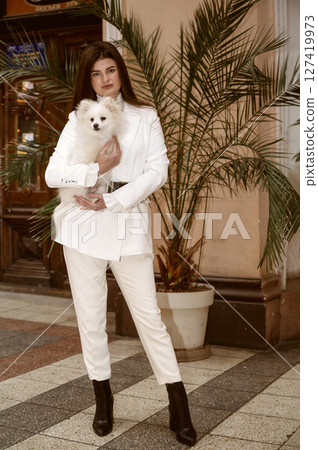 A person standing in front of a building, The girl is holding a spitz dog. 127419973