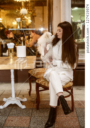 A person standing in front of a building, The girl is holding a spitz dog. 127419974