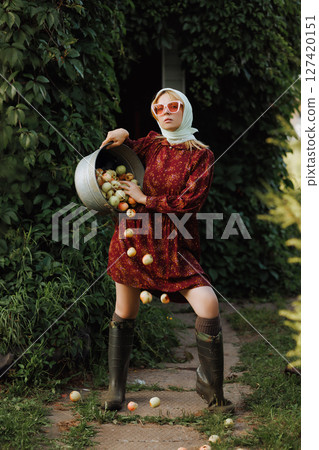 A fashionable woman in a red dress is holding a bucket full of apples 127420151