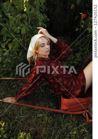 A fashionable woman poses on a red wheelbarrow in the garden 127420152