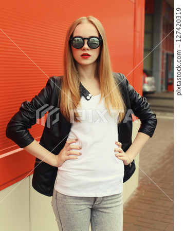 Stylish young woman standing in black leather jacket, sunglasses, modern blonde girl posing in city 127420319