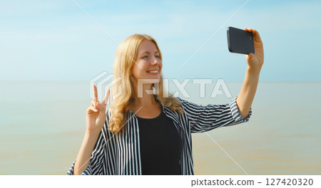 Happy cheerful young woman smiling taking selfie with smartphone on the beach, joyful girl on sea 127420320