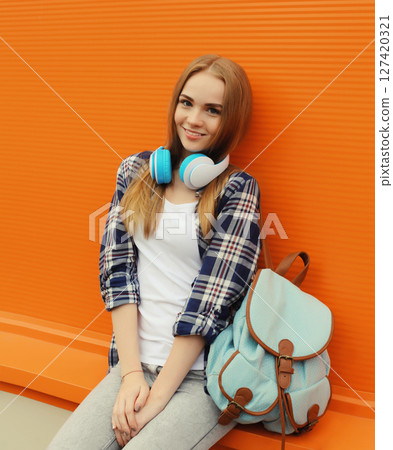 happy young woman listening to music with headphones, modern teenage girl with backpack in the city 127420321