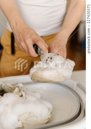 Close-up vertical cropped shot of housewife washing dirty white sneakers with cleaning foam and brush in basin, applying detergent on footwear, doing housework and chores, close-up. Close-up vertical cropped shot of housewife washing dirty white sneakers with cleaning foam and brush in basin, applying detergent on footwear, doing housework and chores, close-up. 127420371