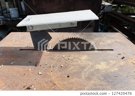 Close up of a circular saw blade cutting through wood, creating sawdust and debris on a rusty metal table in a woodworking workshop, highlighting the tools and processes involved in carpentry Close up of a circular saw blade cutting through wood, creating sawdust and debris on a rusty metal table in a woodworking workshop, highlighting the tools and processes involved in carpentry 127420476