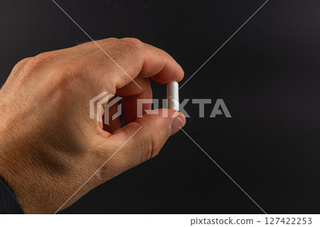 Person holds a small white capsule with one hand 127422253