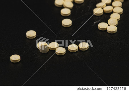 Yellow tablets scattered on a black surface in a clinical setting 127422256