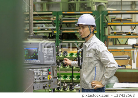 A worker operating a machine on a factory control panel A worker operating a machine on a factory control panel 127422568