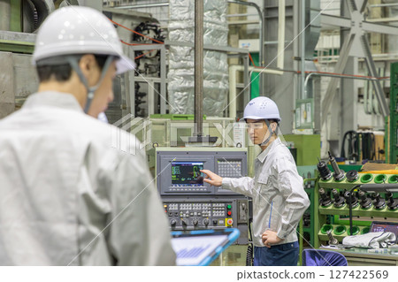 A worker operating a machine on a factory control panel A worker operating a machine on a factory control panel 127422569