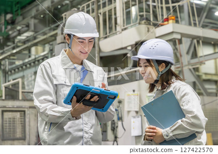 Male and female workers inspecting factory machines with a tablet 127422570