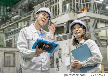 Male and female workers inspecting factory machines with a tablet 127422571