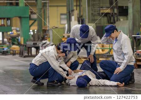 A group of people providing medical assistance to a worker who collapsed at a factory A group of people providing medical assistance to a worker who collapsed at a factory 127422753