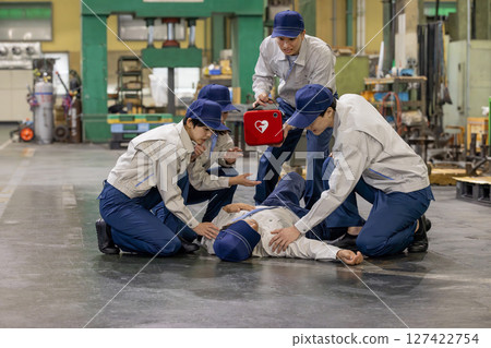 A group of people using an AED to help a worker who collapsed at a factory 127422754