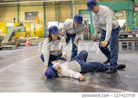 A colleague helps a collapsed worker at a factory 127422759