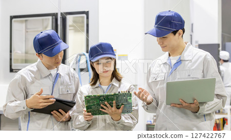 Male and female workers inspecting products using gadgets in factory 127422767