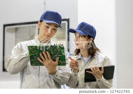 Male and female workers inspecting products using a tablet in a factory 127422793