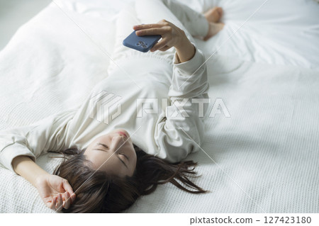 一名婦女在床上的看一個智能手機 一名婦女在床上的看一個智能手機 127423180