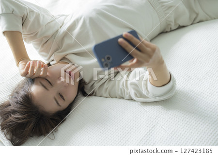 一名婦女在床上的看一個智能手機 一名婦女在床上的看一個智能手機 127423185
